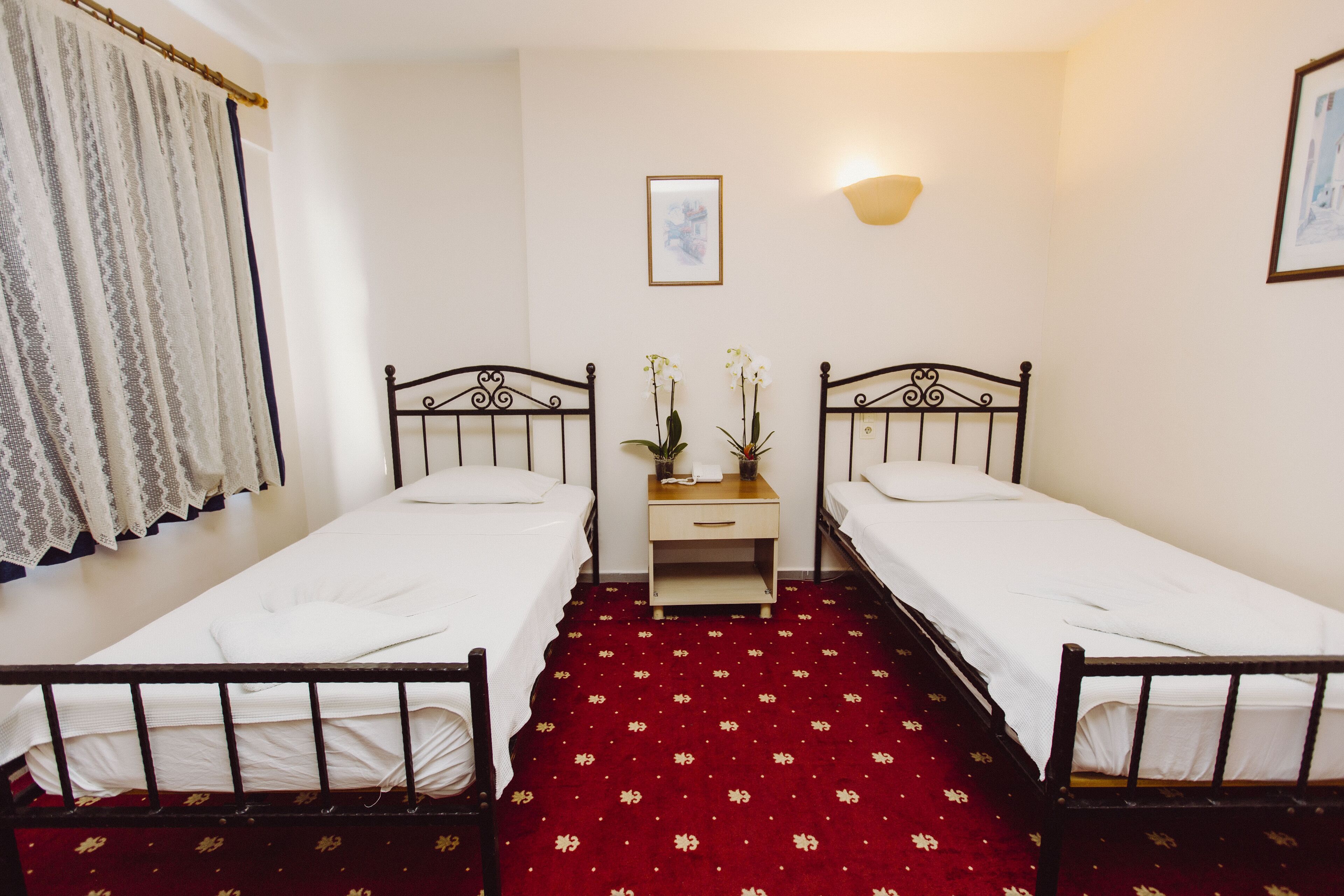 Una habitación con dos camas individuales, una mesita de noche con lámpara y un cuadro en la pared.