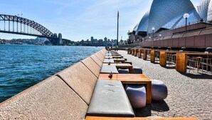 Un paseo marítimo con zonas de estar y vistas a la Ópera de Sydney y al Puente de Sydney.