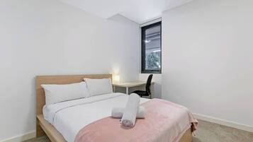 A bedroom with a bed, a desk, and a window.