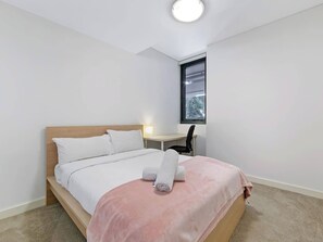 A bedroom with a bed, a desk, and a window.