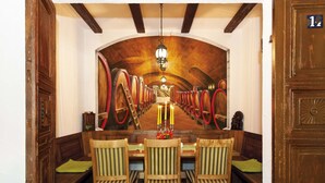 A dining area with wooden chairs and a table, a chandelier, and a mural of wine barrels on the wall. - Kurparkstübl Bad Schandau (Bad Schandau)