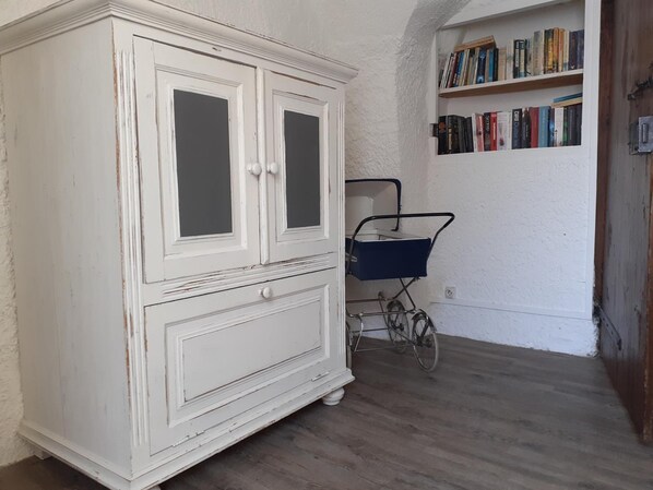Ein weißer Schrank mit zwei Türen, ein kleiner blauer Wagen und ein Bücherregal mit Büchern.