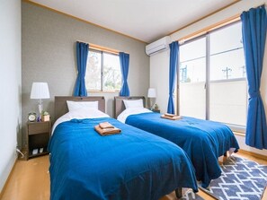 Ein Hotelzimmer mit zwei Betten, einem Fenster mit Vorhängen, einer Klimaanlage, einem Nachttisch mit Lampe und einem gemusterten Teppich.