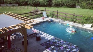 Piscina con cubierta de madera, sillas de descanso y vista a una colina boscosa.