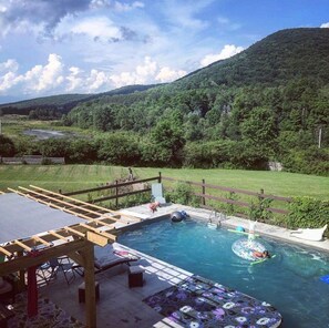 A swimming pool with a wooden deck, lounge chairs, and a view of a forested hill. - Heated Pool, hot tub, Pickleball, Sleeps 10, Seneca Wine Trail nearby (Beaver Dams)