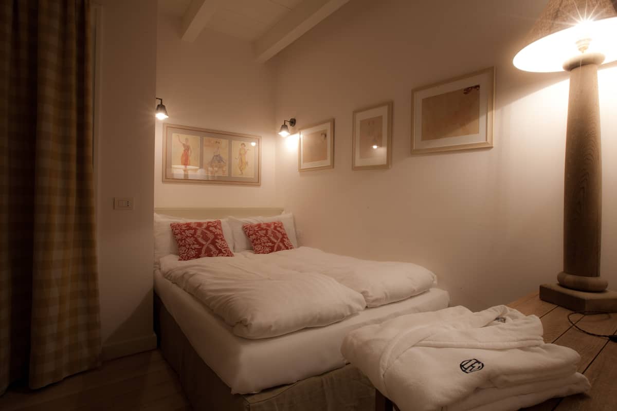 Una habitación de hotel con cama, mesita de noche, lámpara y cuadros en las paredes.