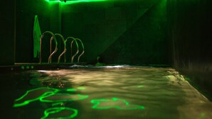 A dimly lit room with a green-lit pool, a towel rack, and a visible shower area. - Les Fleurs Bleues chalets (Livigno)