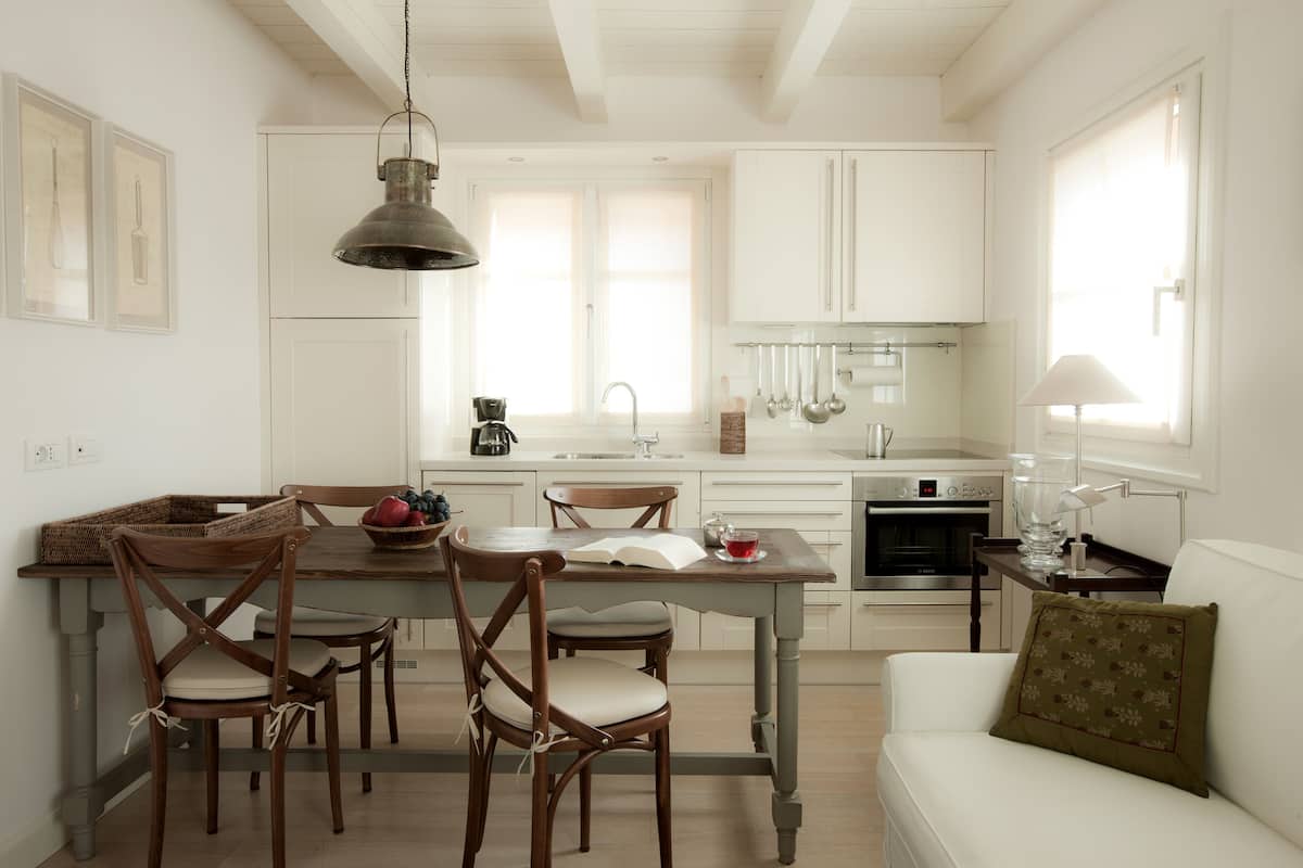 Una cocina moderna con armarios blancos, una mesa de comedor con sillas y un sofá blanco con un cojín.