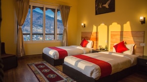 Une chambre d’hôtel avec deux lits, une vue sur les montagnes, un tableau représentant un oiseau et une couvre-lit rouge et blanche.