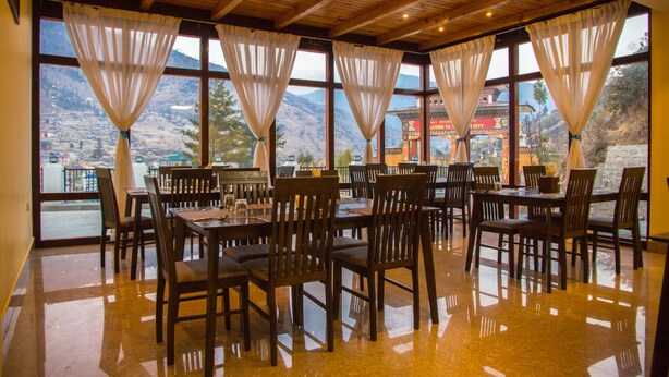 Un restaurant avec des tables et des chaises en bois, de grandes fenêtres avec des rideaux et une vue sur les montagnes.