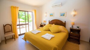 Habitación de hotel con una cama grande, una silla de madera, una mesita de noche con lámpara y una ventana con cortinas.