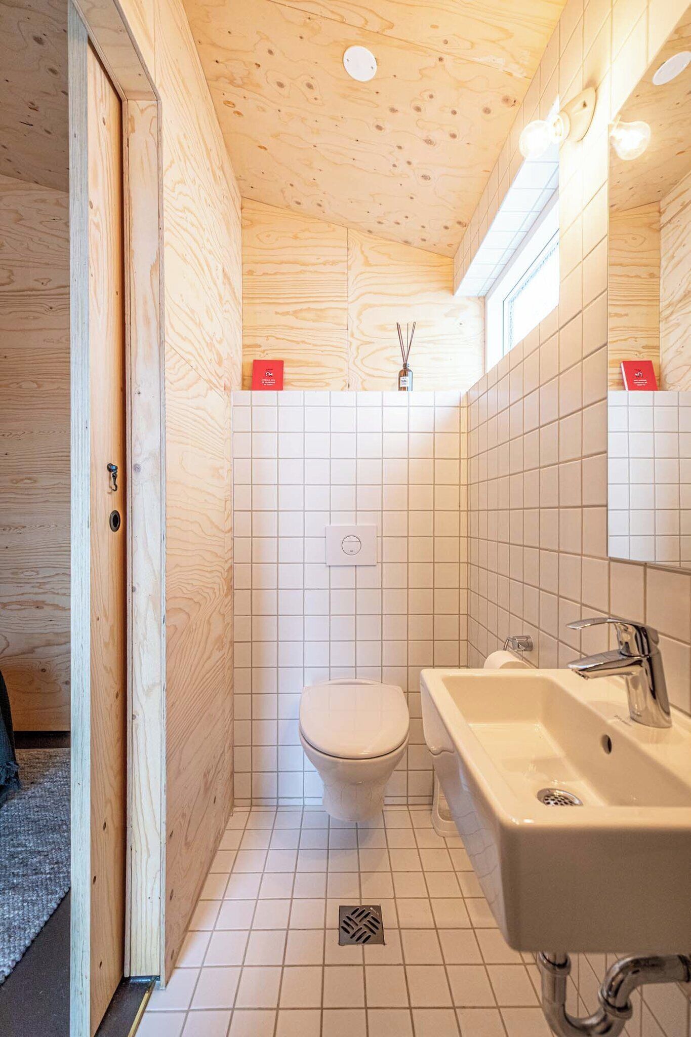A compact bathroom with a wooden ceiling, white tiled walls, a white toilet, and a sink with a mirror.