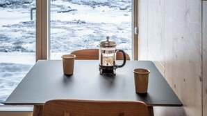 Un comedor con mesa, sillas, una cafetera y vistas a un paisaje nevado a través de un ventanal grande.
