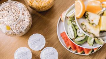 Una mesa con un tazón de frutas en rodajas, un plato con vasitos de yogur y un tarro de avena.