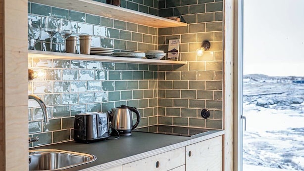 Una cocina moderna con armarios de madera, encimera negra y salpicadero de azulejos verdes.