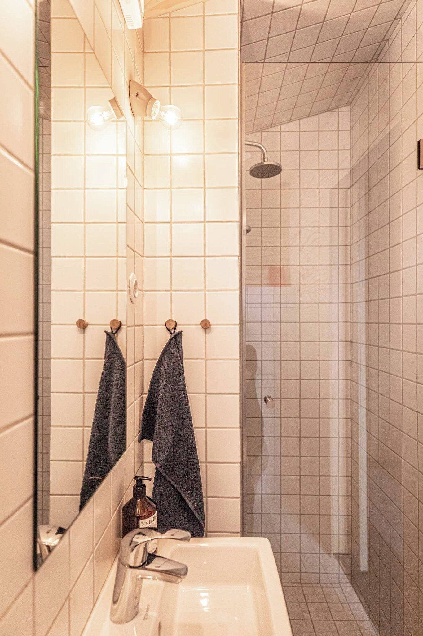 A bathroom with a sink, mirror, two towels, a bottle of lotion, and a shower area.