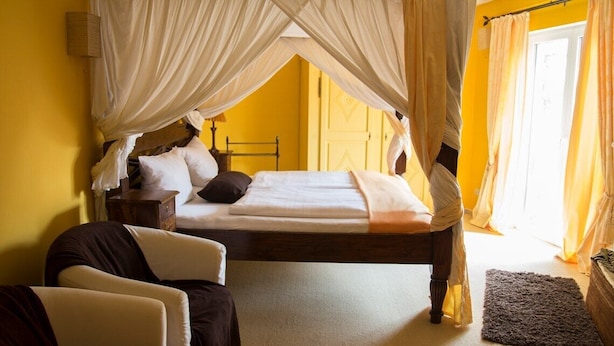 A bed with a canopy, a bedside table, and a chair in a room with yellow walls. - Villa ZOE St Wendel (Sankt Wendel)
