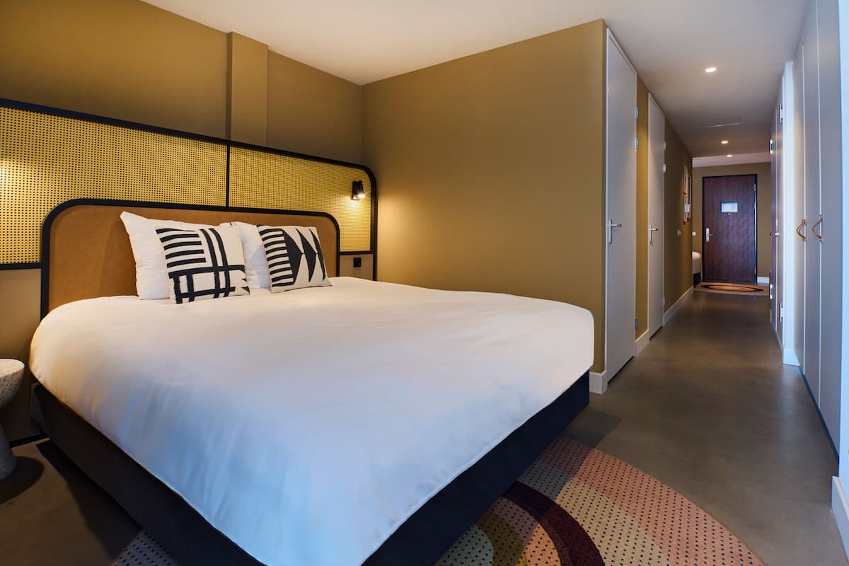 Una habitación de hotel con una cama grande, un cabecero con diseño tejido y un pasillo largo con puertas.