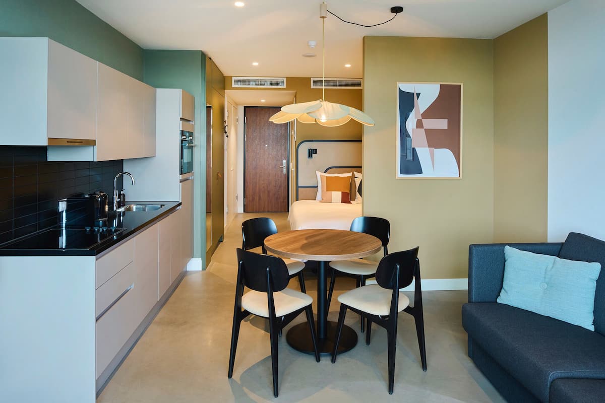 Un espacio habitable compacto con kitchenette, una zona de comedor con una mesa redonda y sillas, un sofá y una cama al fondo.