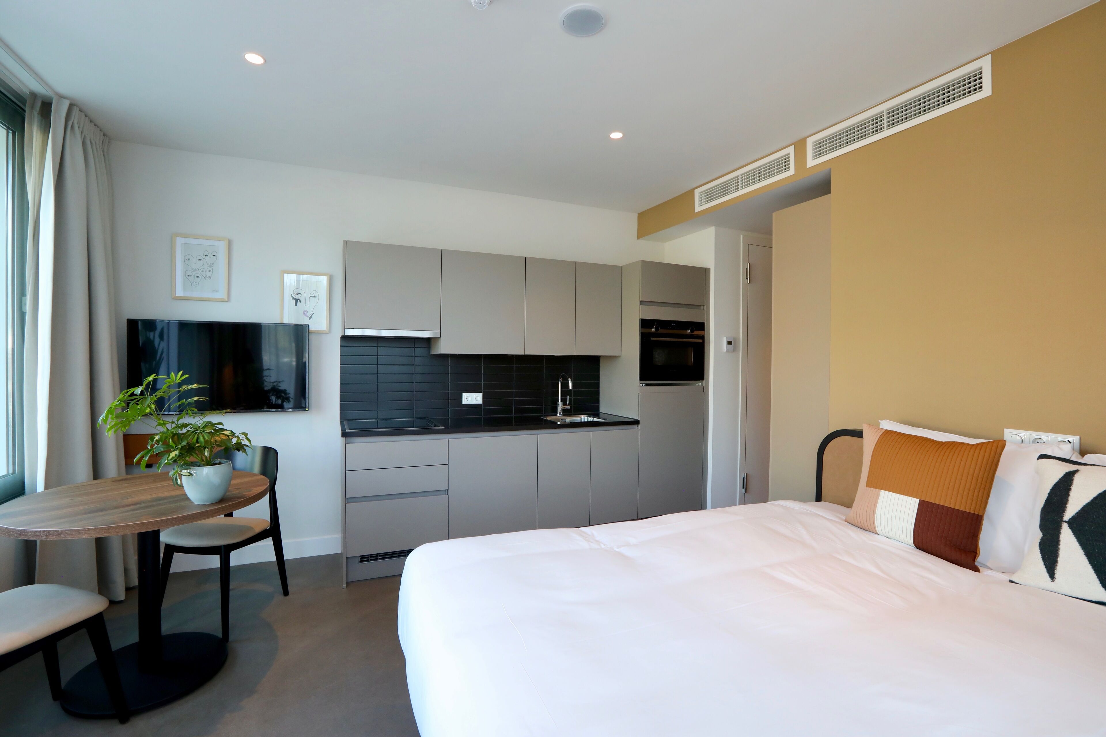 Une chambre d’hôtel moderne avec un grand lit, une table à manger avec des chaises, un petit coin cuisine et une plante en pot.