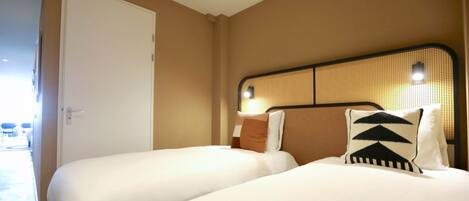 Habitación de hotel con dos camas, una puerta y un cabecero trenzado.