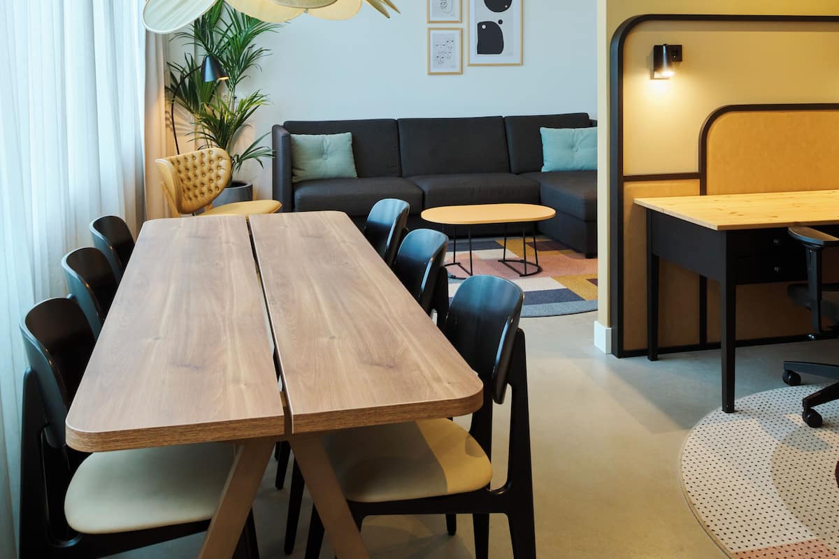 Una habitación de hotel moderna con una mesa de comedor de madera, sillas negras, un sofá y una pequeña mesa redonda.
