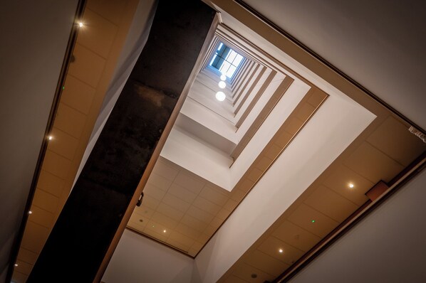 A multi-level interior with a central staircase, recessed lighting, and a view of the upper floor through a glass door. - Cityden BoLo District (Amsterdam)