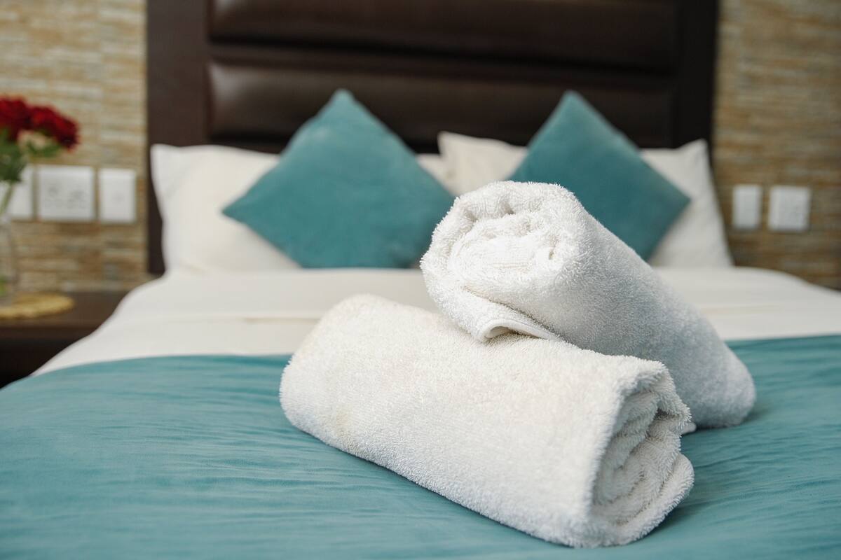 A neatly made bed with white towels and teal bedding, a brown headboard, and teal pillows.
