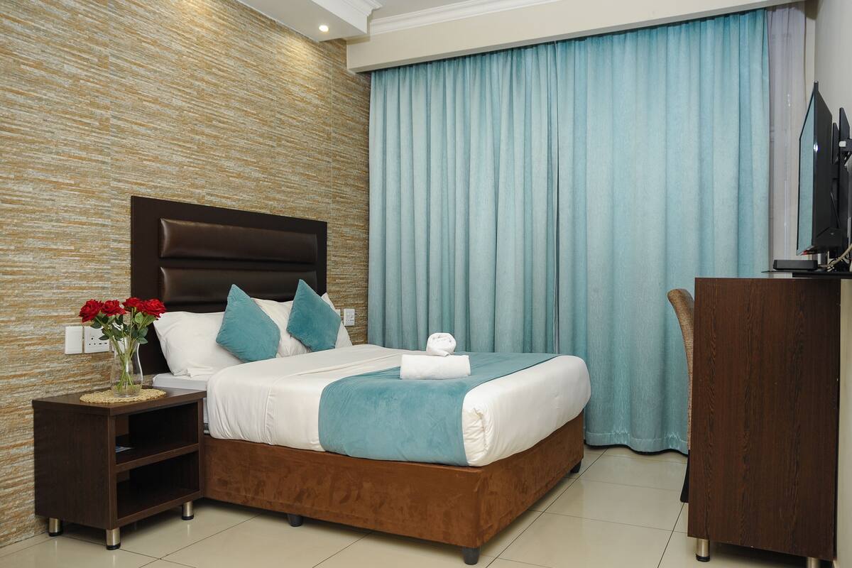 A hotel room with a bed, nightstand, and a desk with a TV.