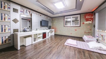 Ein modernes Hotelzimmer mit Holzboden, einem Schreibtisch mit Computer, einem Flachbildfernseher und Bücherregalen voller Bücher.