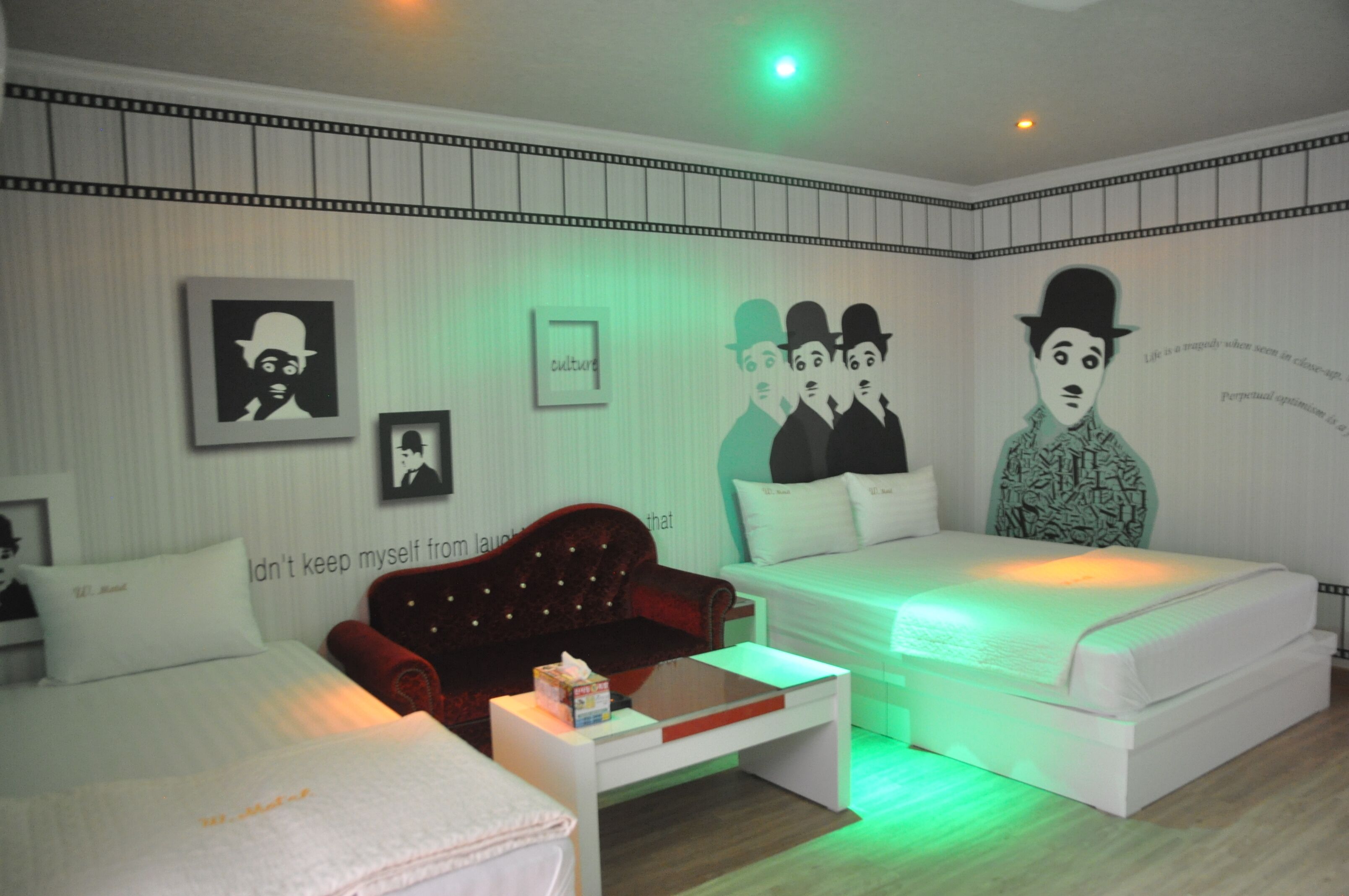 A hotel room with a bed, a red sofa, a white bedside table, and a small table with a box.