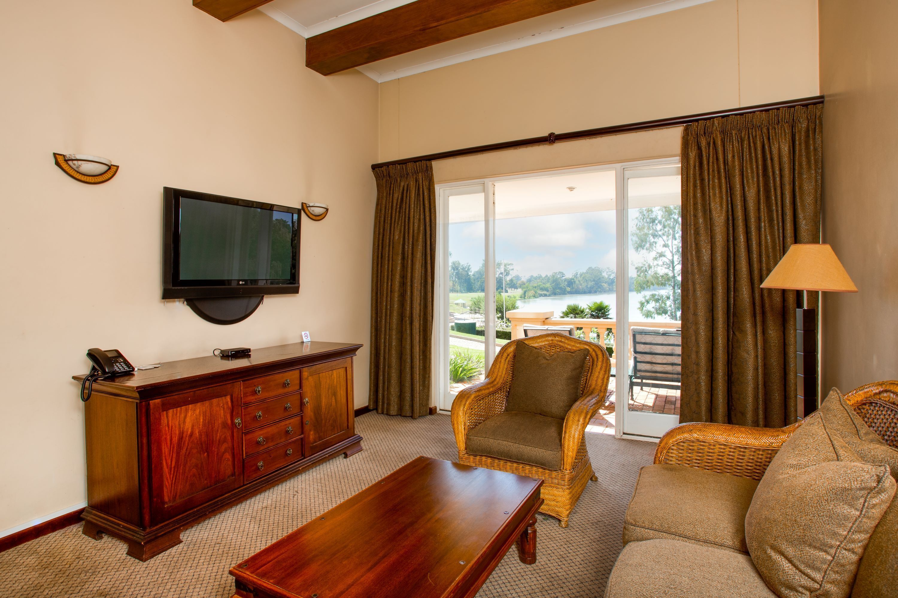 A living room with a television, a wooden cabinet, a wicker armchair, a sofa, and a view of the outdoors through a sliding glass door.