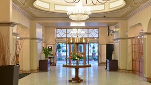 A spacious lobby with a chandelier, a round table with flowers, and a view of the outdoors through large windows. - Riviera On Vaal Resort (Vereeniging)