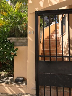 A black metal gate with a number '4' sign, a staircase with patterned tiles, and lush greenery.