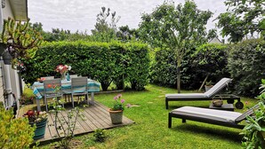 A backyard with a wooden deck, a table with chairs, a lounge chair, and a potted plant. - Cottage Maison Drogou (Porspoder)
