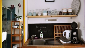 A kitchen with a blackboard displaying "Bienvenue à Postopoder!" and a shelf with various kitchenware and containers. - Cottage Maison Drogou (Porspoder)