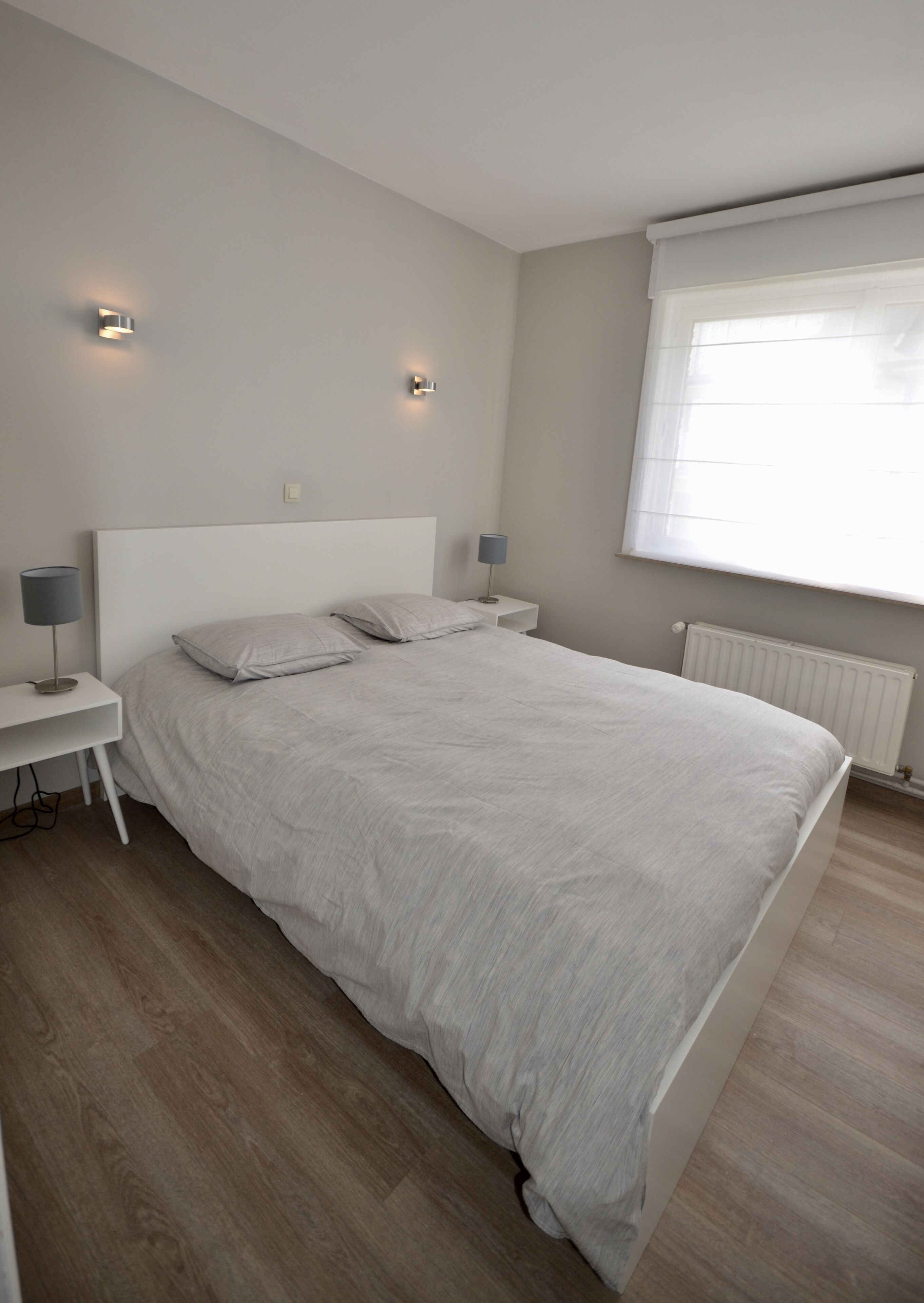 Un dormitorio moderno con una cama grande, dos mesitas de noche y una ventana con persianas.