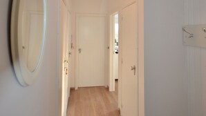 A hallway with wooden flooring, white walls, and doors.