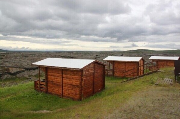A row of wooden cabins with metal roofs, set against a backdrop of rocky terrain and overcast sky. - Hlid Huts (Myvatn)