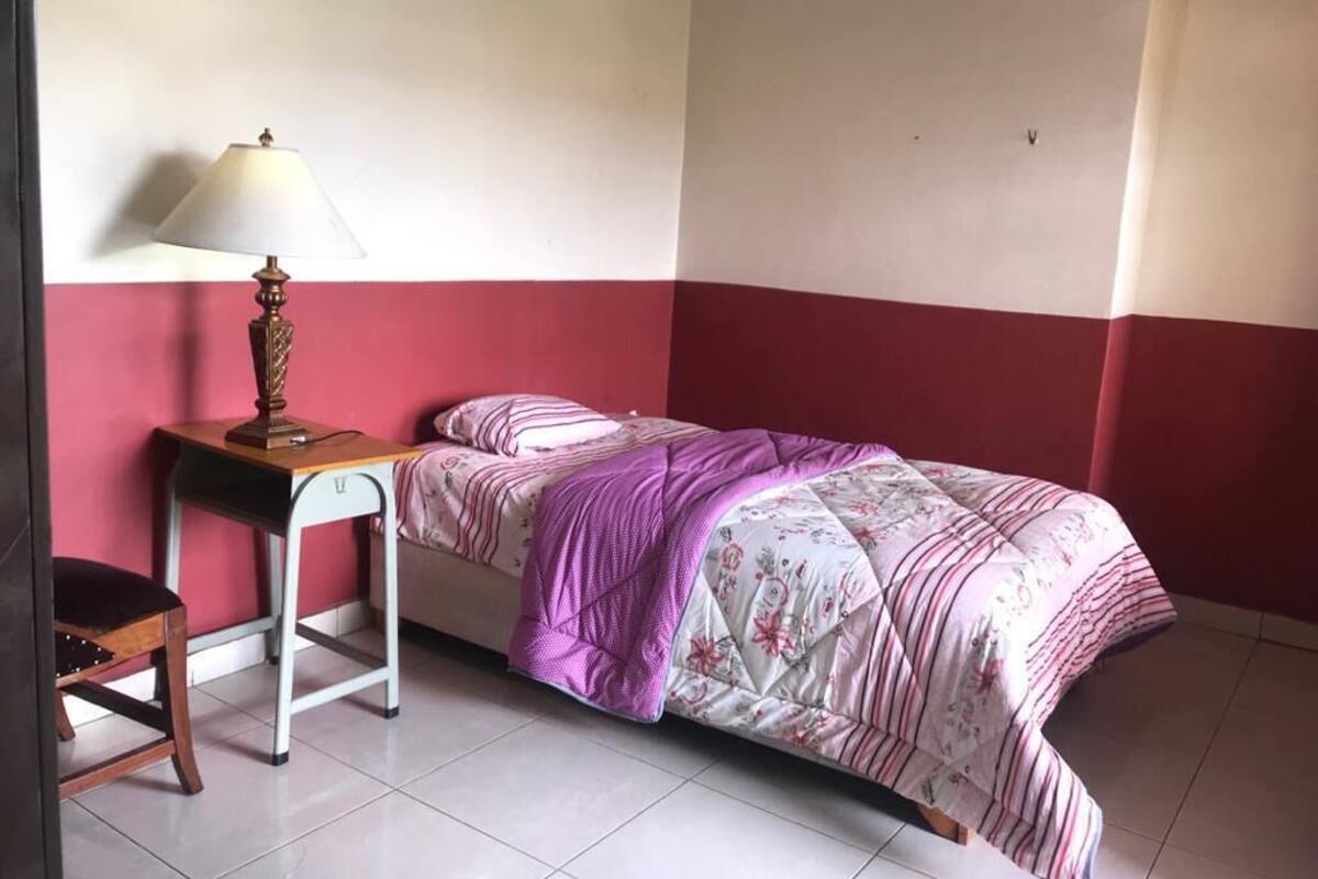 A bedroom with a bed, a nightstand, a lamp, and a chair.