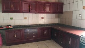 A kitchen with dark wooden cabinets, a granite countertop, and a gas stove. - Rainbow Aparts (Kigali)
