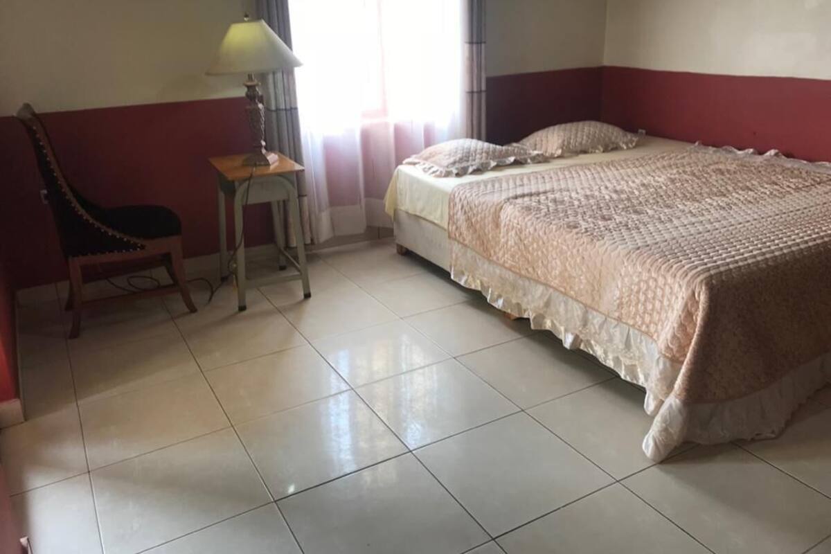A bedroom with a bed, a chair, a lamp, and a window with curtains.