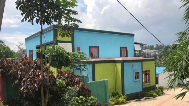 A two-story building with a blue and green facade, surrounded by lush greenery. - Rainbow Aparts (Kigali)