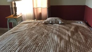 A bed with a textured blanket, a bedside table with a lamp, and a chair. - Rainbow Aparts (Kigali)