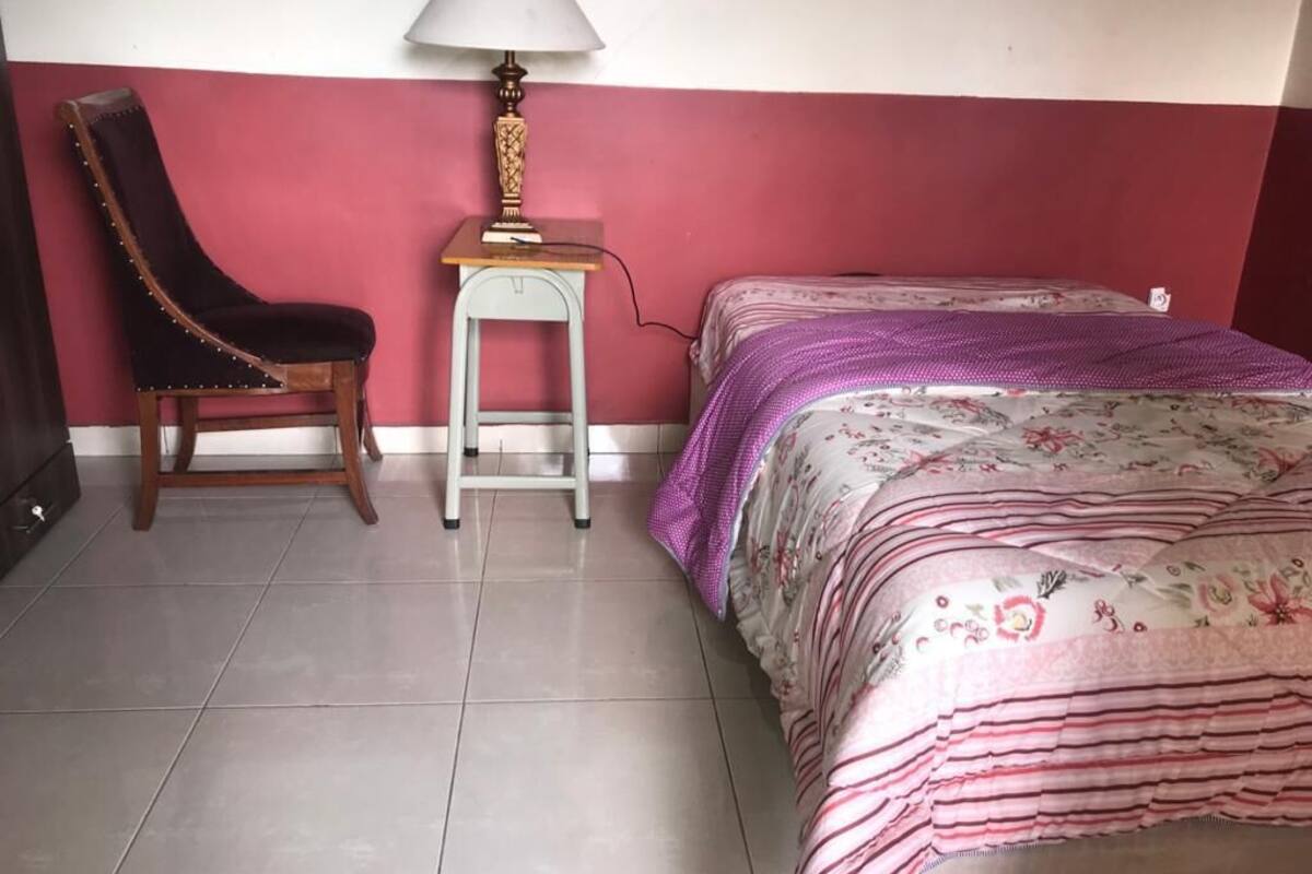 A bedroom with a bed, a chair, a nightstand, and a lamp.
