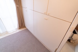 A room with a beige carpet, a white wardrobe with multiple doors, and a window with sheer curtains.