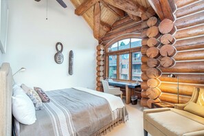 A log cabin bedroom with a bed, a desk, and a chair.