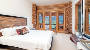Ein Schlafzimmer mit einem großen Bett, einem Holz-Kopfstück, Blick durch eine Glastür und einer Steinwand.
