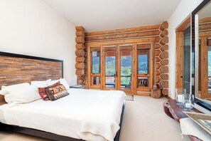 Une chambre avec un grand lit, une tête de lit en bois, une vue à travers une porte vitrée et un mur en pierre.
