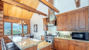 A kitchen with wooden cabinets, granite countertops, a large island with seating, a stainless steel range hood, and a view of the outdoors. - Beautiful Ski-In/Ski-Out Log Townhome with Exceptional Views (Mountain Village)